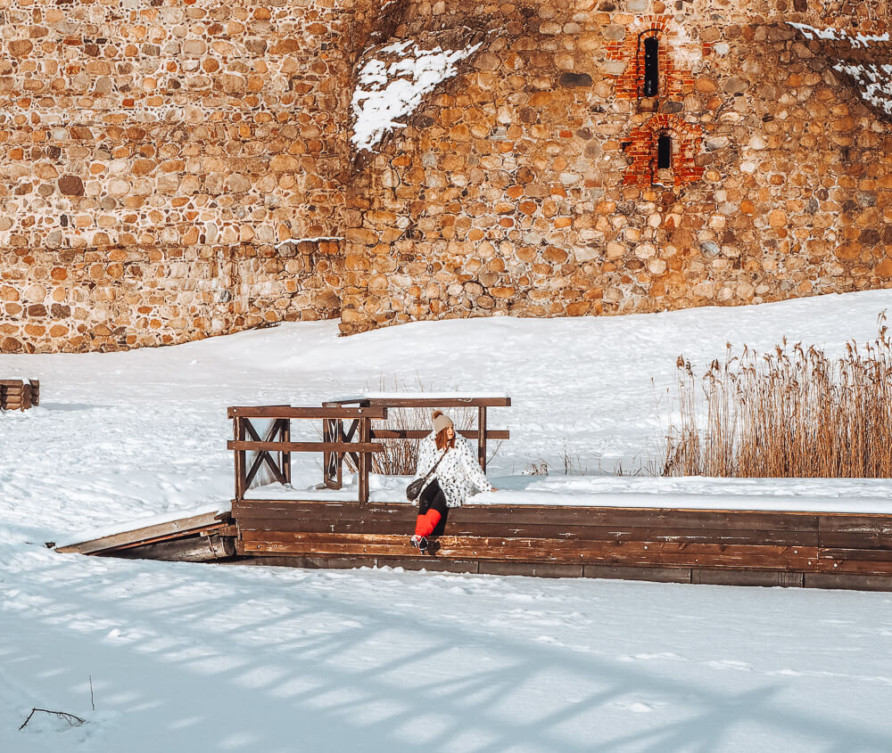Woman wearing red boots sitting on a pier at Trakai Castle in Lithuania