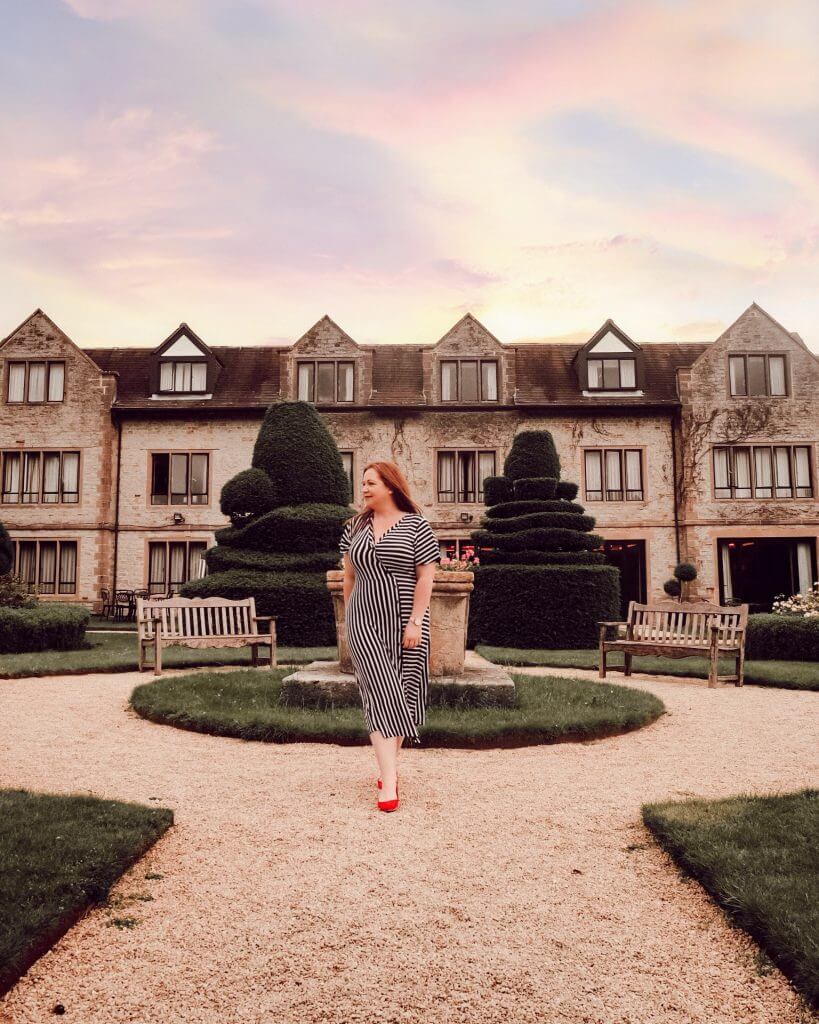 Woman in a striped dress walking in the gardens at Billesley Manor House in the Cotswolds. It is a historic manor house transformed into a luxury hotel in the Cotswolds, blending traditional charm with contemporary comfort.