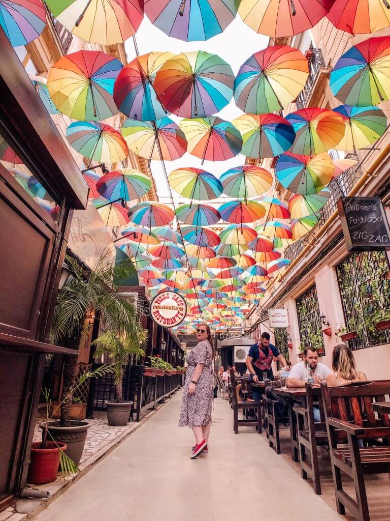Woman standing under a colourful Umbrella sky in Bucharest. The best travel hashtags to use for killer reach. A list of over 250 travel hashtags for Instagram. Read more on www.ouruniquestays.com