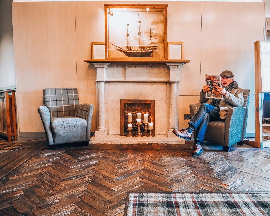 Man sitting in an armchair reading a newspaper beside the fire at Armada Spanish Point Hotel