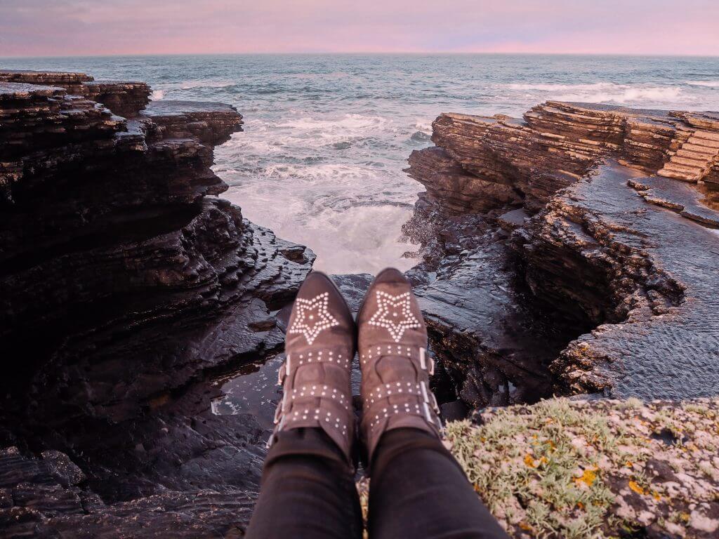 Serene coastline along Kilkee Cliffs, offering peace and solitude. Legs wearing star studded boots hanging over a cliff edge on the Irish coast.