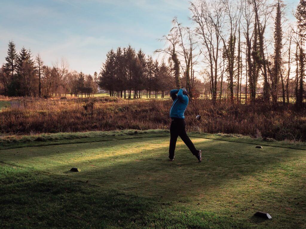 Man in blue top practicing his golf swing.