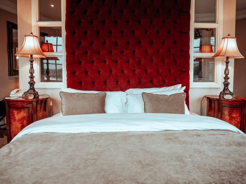 Luxurious hotel bedroom. Large double bed with a red velvet bead head and two lit lamps on either side