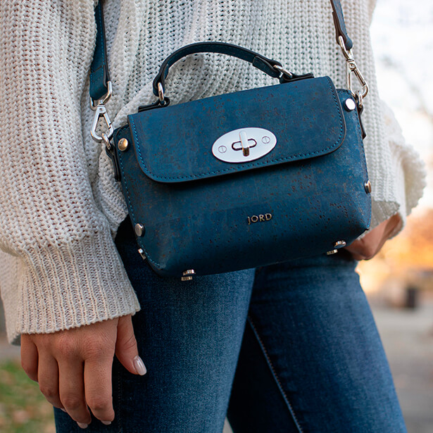 Woman wearing a peacock blue and gold vegan leather handbag designed by JORD