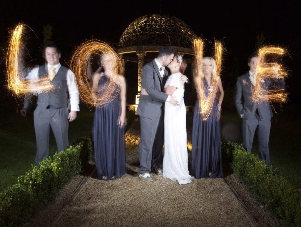 Couple on their wedding day surrounded by sparklers that spell the word Love