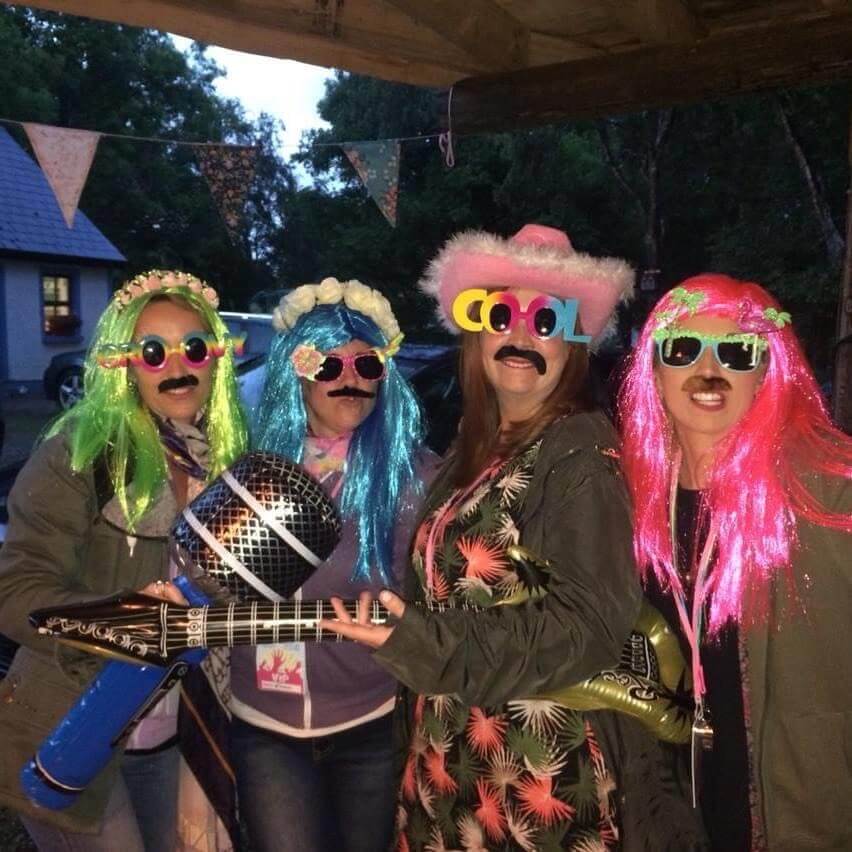 Four girls all dressed up in crazy festival gear wearing multicoloured wigs at a festival themed hen party