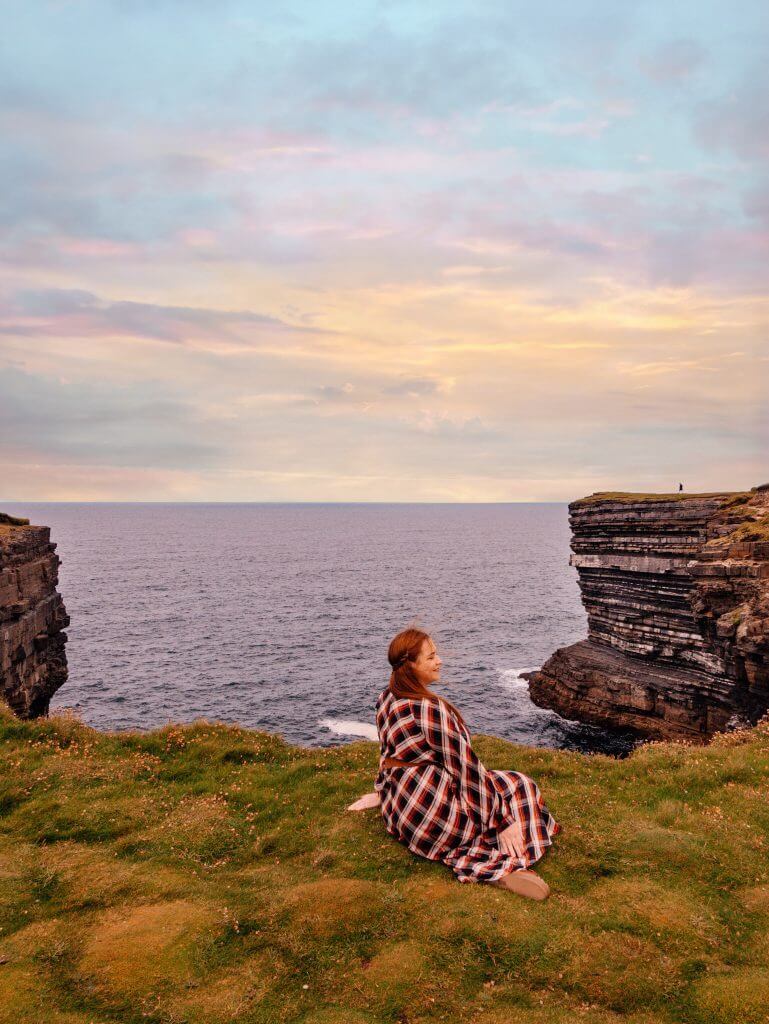 Woman in a tartan dress sitting at the cliffs of Downpatrick Head Mayo