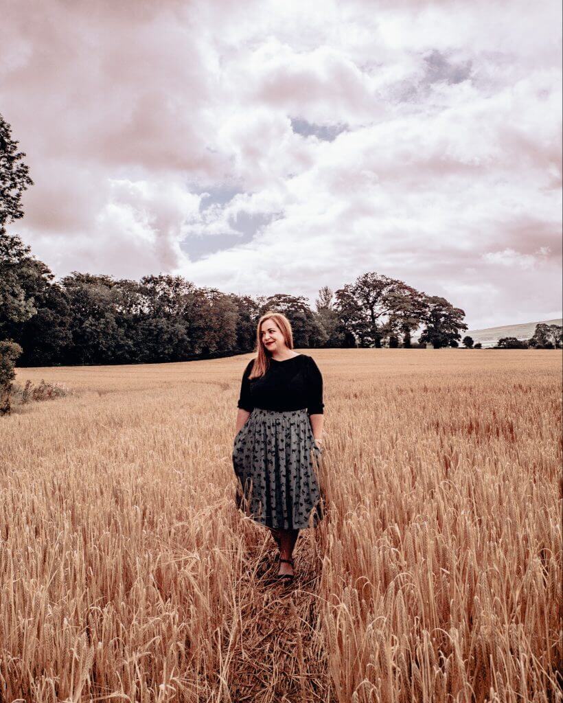 Woman in a black top and green skirt walking through a hayfield in Donegal perfect for your Ireland staycation