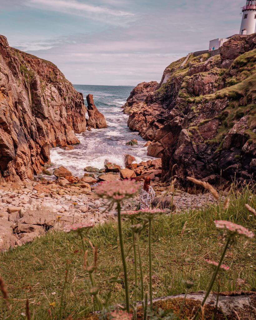 Woman standing on a beach looking up at Fanad Lighthouse in County Donegal Ireland