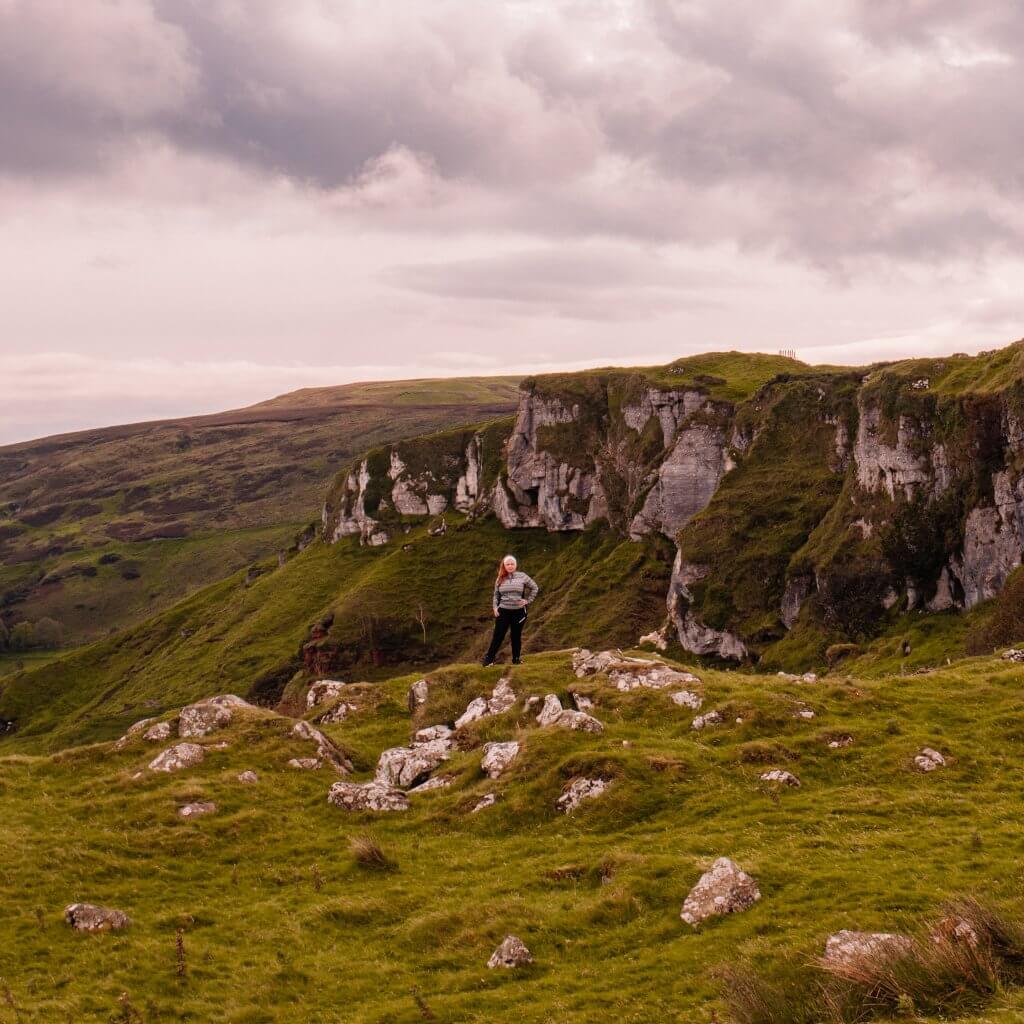Woman standing against the dramatic backdrop of the cliffs of Murlough Bay an iconic filming location for Game of Thrones in Ireland