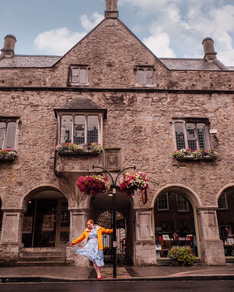 Woman in a yellow raincoat twirling around a lamp post outside Rothe House in Kilkenny Ireland