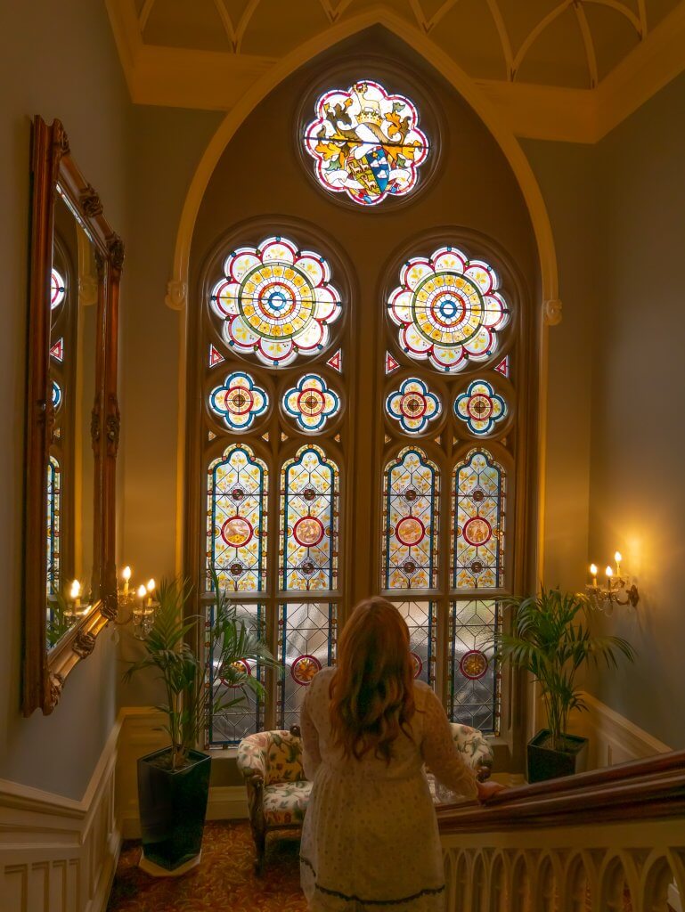 Woman looking at a stain glass window on the staircase of the Culloden Estate and Spa