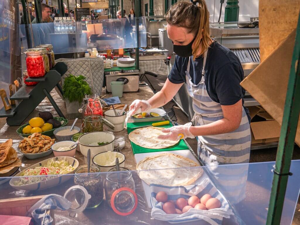 Woman serving food from a market stall at St George's market on a walking tour Belfast