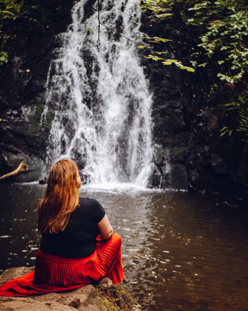 Women in a red skirt sitting at Glenoe waterfall in Antrim Northern Ireland