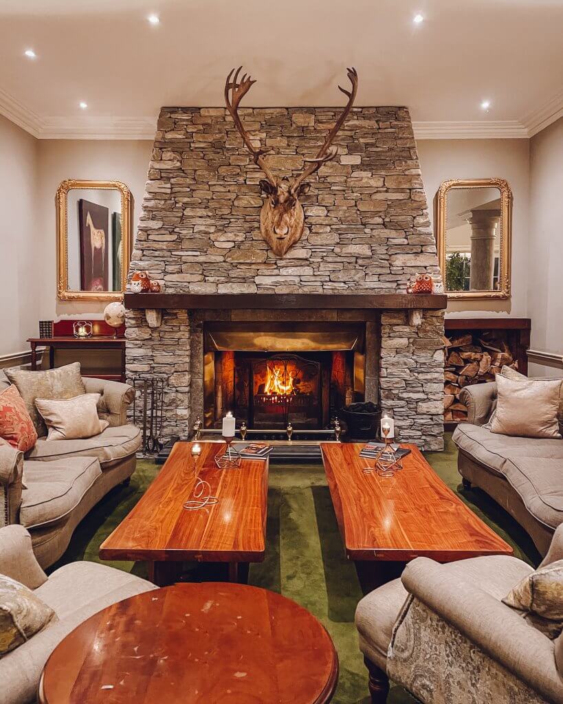 Cosy fireplace in reception at Sheen Falls Lodge, creating a warm and inviting atmosphere for guests to relax. The decor resembles that of a country hunting lodge.