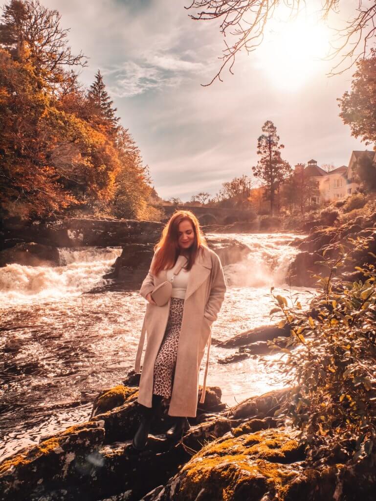 Woman standing near Sheen falls waterfall in Kenmare Kerry. Sheen Falls Lodge's iconic waterfall, a mesmerizing natural wonder that adds to the hotel's charm.