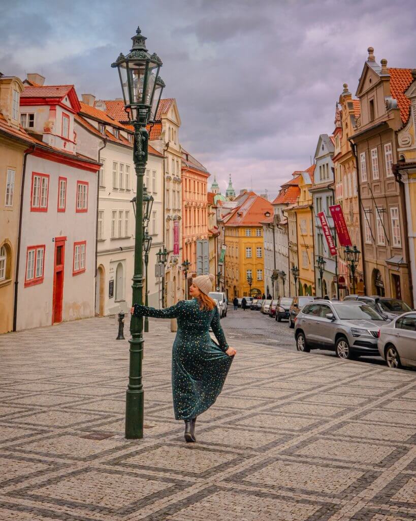 Woman in a green velvet dress standing beside a green lampost in Nerudova Street in Prague