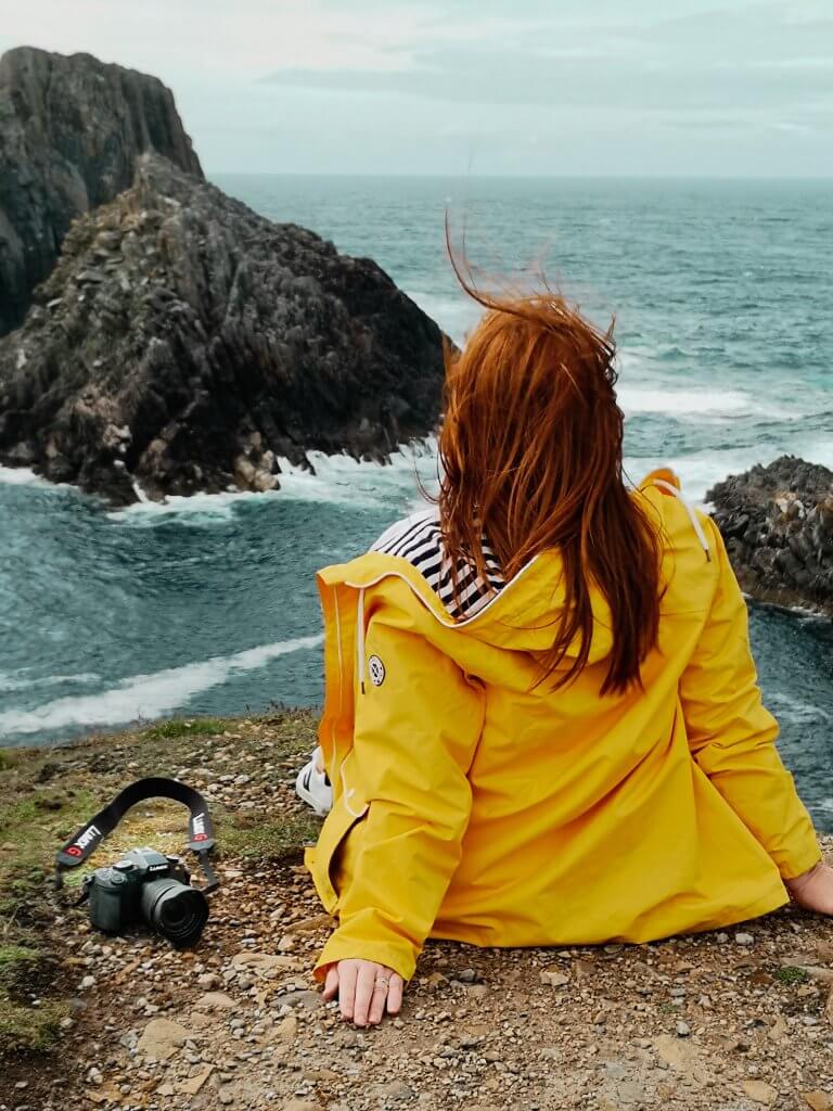 Woman sitting on a cliff at Malin Head with her travel must have a Panasonic Lumix G80 camera