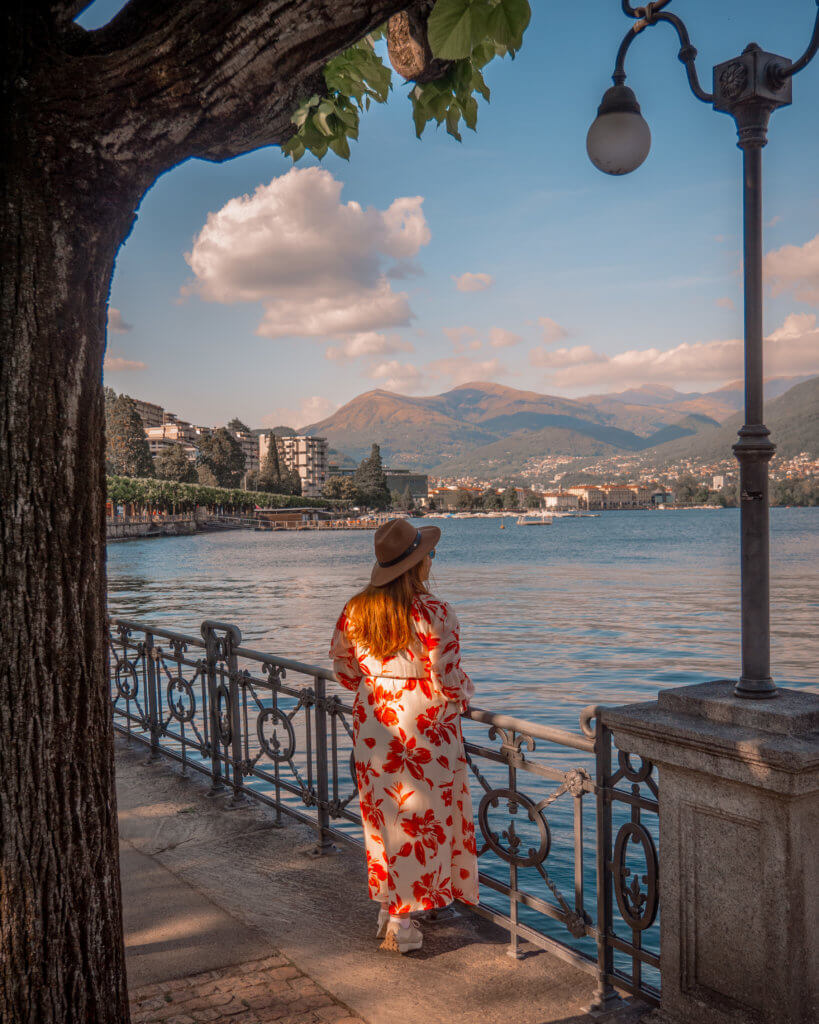 Nicola Lavin, travel writer with Our Unique Stays, wears a floral dress and looks at the view of Lake Lugano in Switzerland