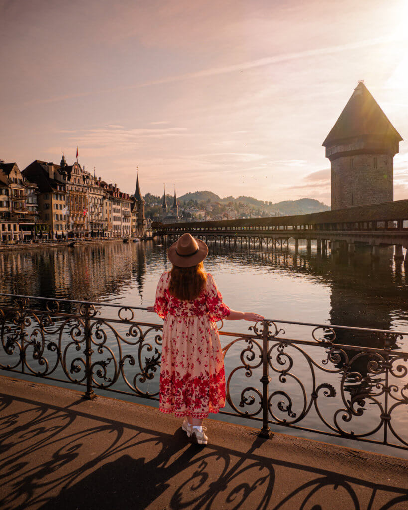 Nicola Lavin, a travel writer with Our Unique Stays, is standing on a bridge in Lucerne at sunrise looking at the wooden chapel bridge
