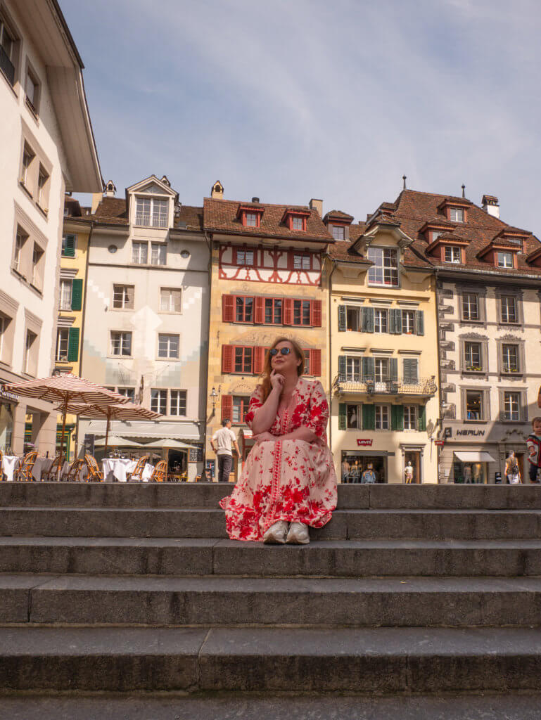 Nicola Lavin, travel blogger with Our Unique Stays, sits on the steps of Kornmarkt in Lucerne Old Town during one day in Lucerne.