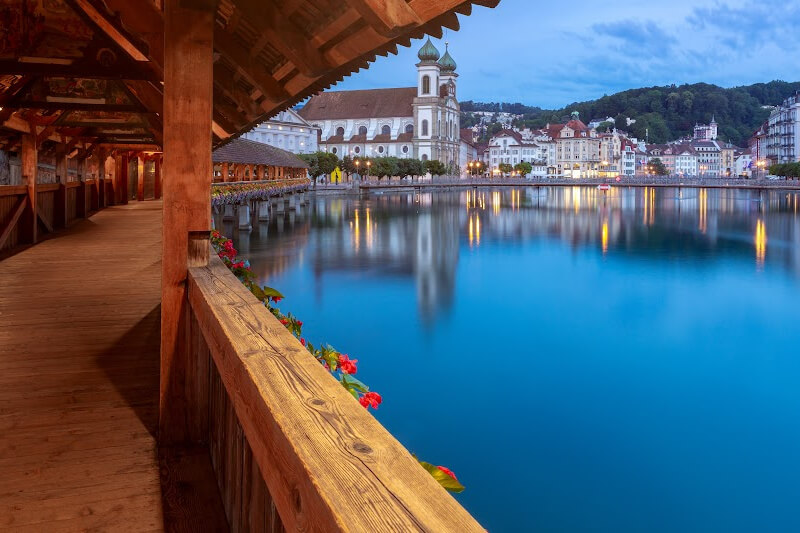 Jesuit Church and wooden Chapel Bridge in Lucerne at dusk.