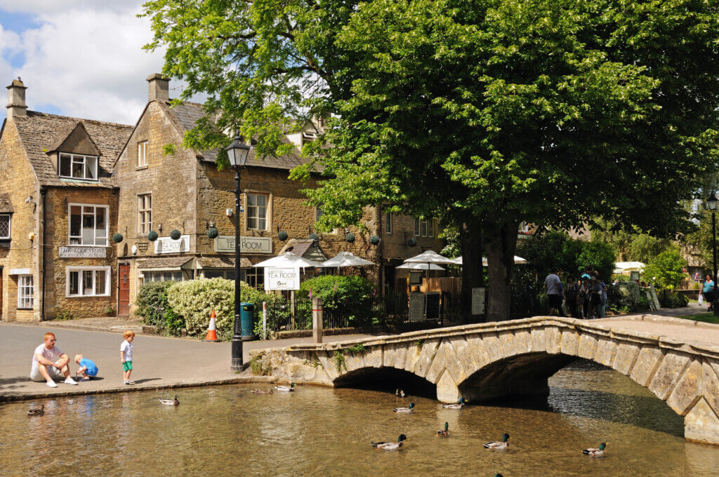 Bourton on the Water, United Kingdom: Father with two children looking at the ducks on the River Windrush with tea-rooms to the rear, Bourton on the Water, Gloucestershire, England, UK, Western Europe.