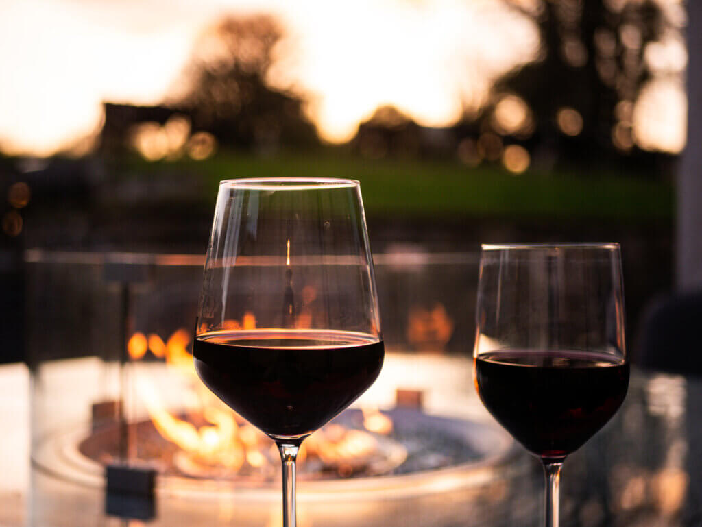 Two glasses of red wine with the backdrop of an outdoor firepit.