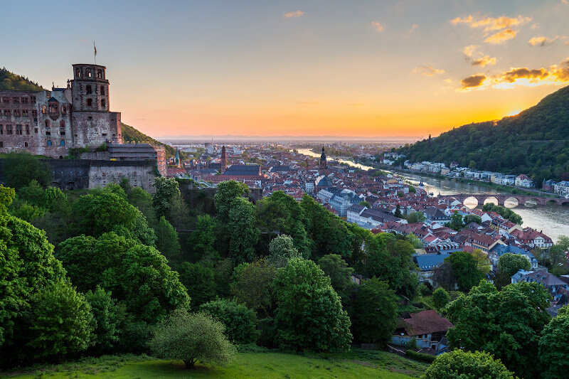 Sunset over Heidelberg, casting a warm glow on the Neckar River and surrounding hills.