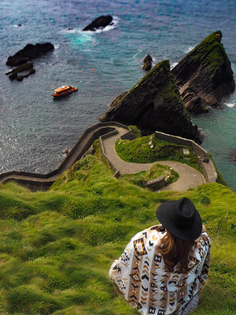 Woman wrapped in a blanket and wearing a black hat looks out at the picturesque Dunquin Pier in Dingle, Kerry, Ireland.