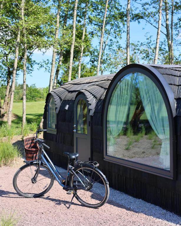 Exterior view of Ballygarry Estate’s luxury cabins in Ireland surrounded by trees and morning light. A blue bicycle with a rustic picnic basket is parked outside.