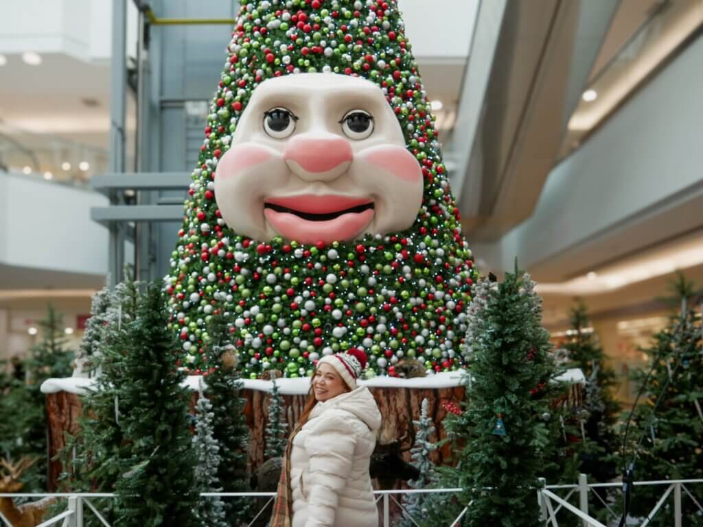 A woman in a white coat and knitted hat and gloves visiting Woody the Talking Christmas Tree in Mic Mac Mall in Halifax, Nova Scotia at Christmas