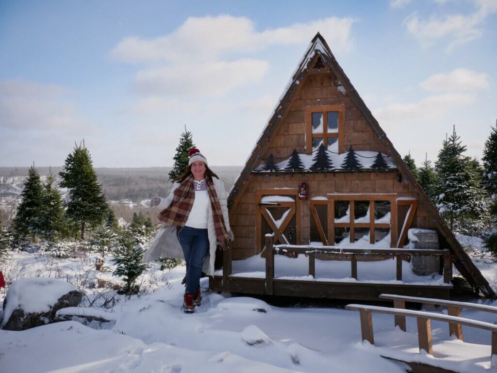 Woman wearing a winter coat and hat and scarf standing at Twig's Chalet on Ruby's Trail in New Ross, Nova Scotia.