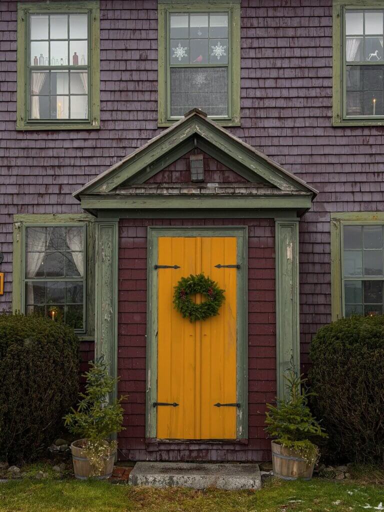 Cute wooden house with a yellow door adorned with a Christmas wreath in Shelburne, Nova Scotia.