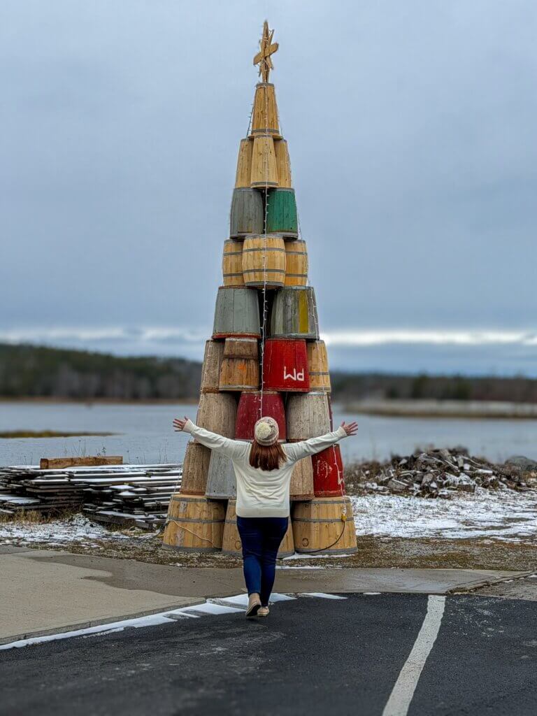 Woman stands with her arms raised in front of a barrel Christmas tree in Shelburne Nova Scotia
