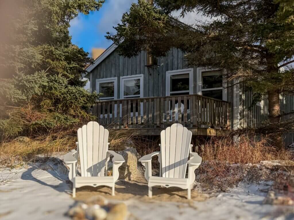 The exterior of Crow's Nest cottage at Oceanstone retreat near Peggy's Cove in Nova Scotia. Two white deck chairs sit outside.