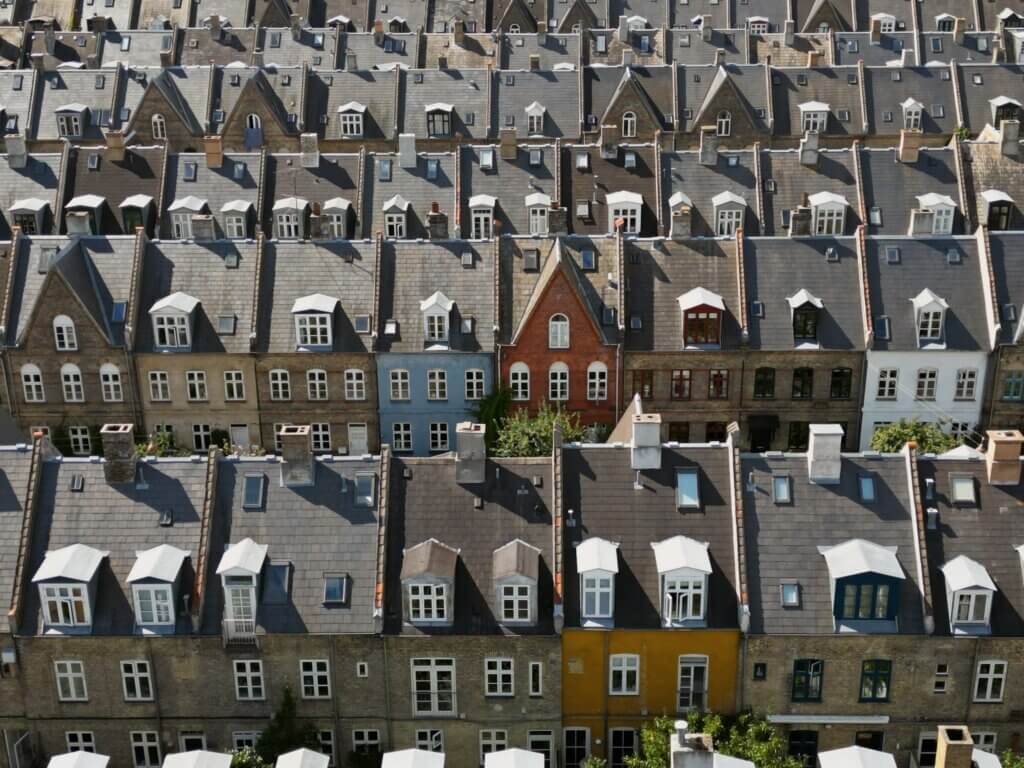 Elevated view looking down at rows of historic terraced townhouses with dark slate pitched roofs, white dormer windows, and colourful brick facades in Copenhagen.