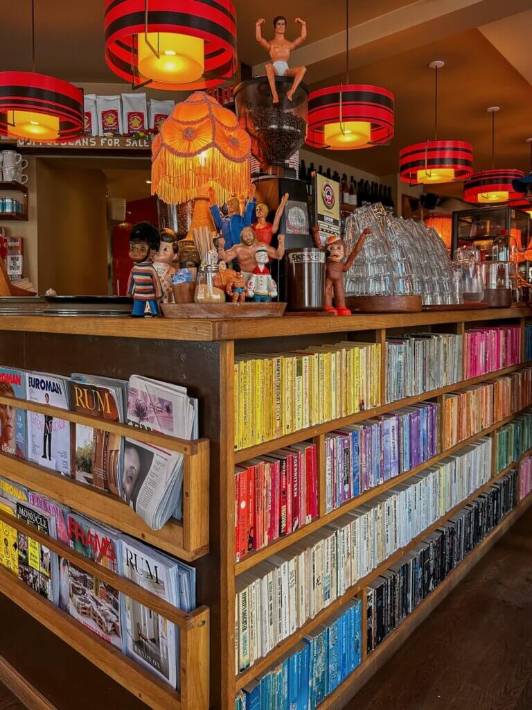Vibrant wooden cafe counter lined with color-coordinated bookshelves and magazines, decorated with retro lamps, action figures, and quirky vintage trinkets at Laundromat Café in Copenhagen.